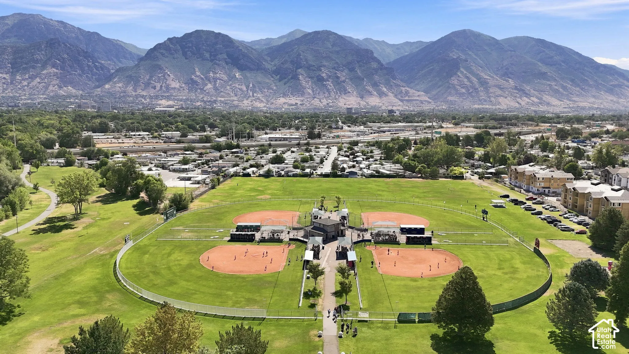 Expansive park grounds featuring four baseball diamonds, manicured grass, paved pathways, and an prominent mountain backdrop