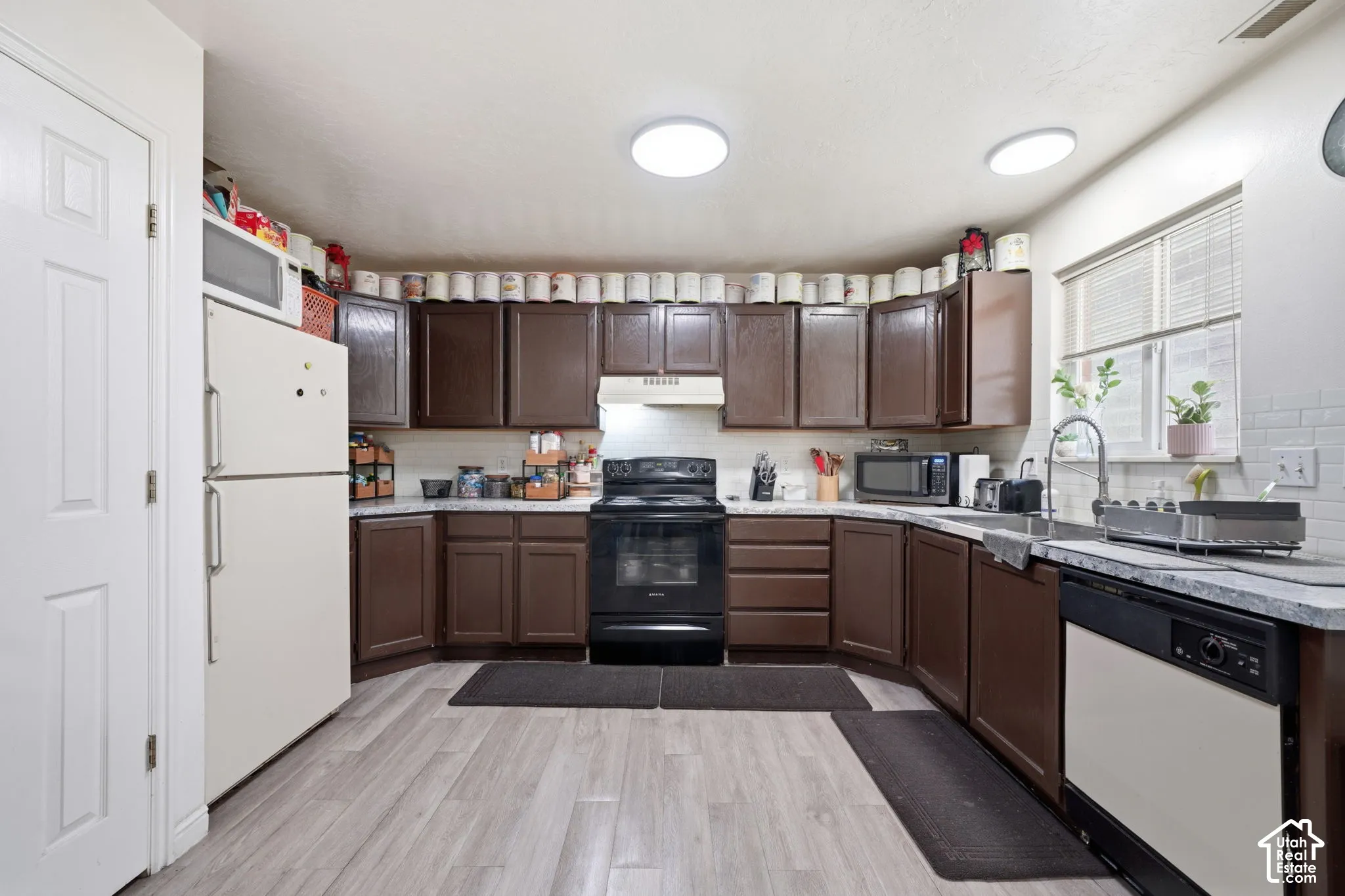 Kitchen featuring dark wood-finish cabinetry, stone-patterned countertops, subway tile backsplash, light wood-finish flooring, and a stainless steel kitchen faucet