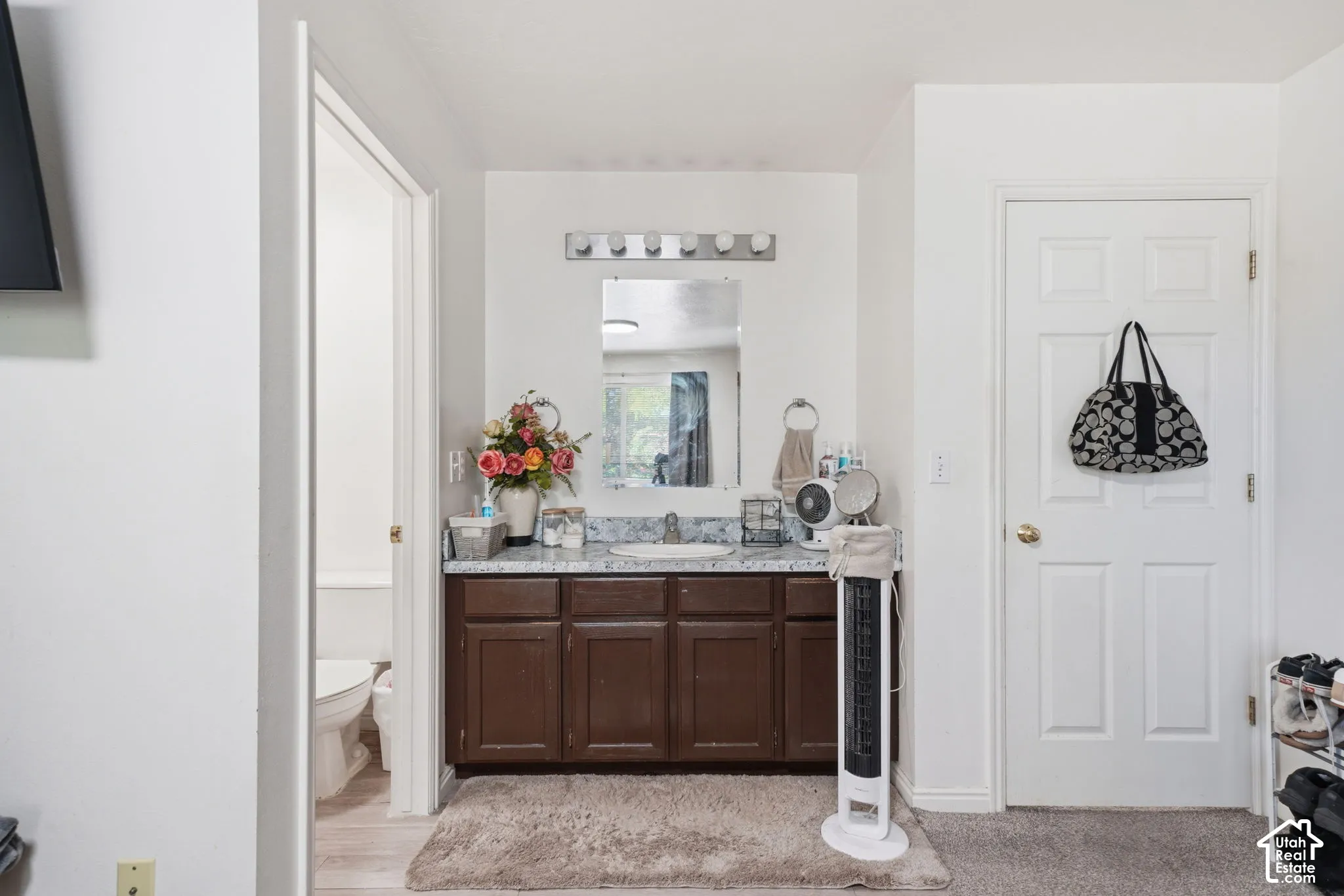 Bathroom vanity featuring dark wood-finish cabinetry, stone-composite countertop, oval undermount sink, wall-mounted mirror, and multi-bulb vanity light fixture
