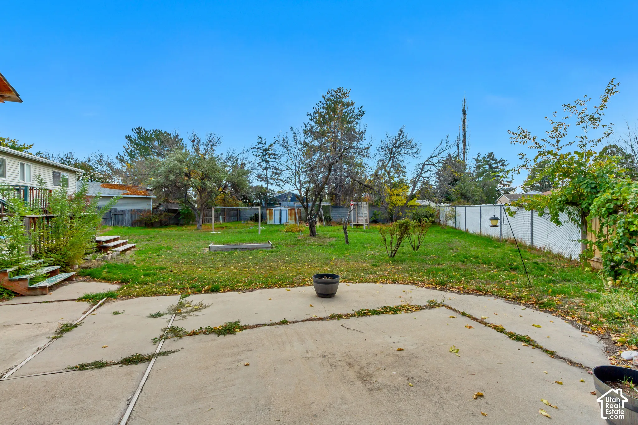 Spacious backyard featuring a concrete patio, wood deck, fenced perimeter, and mature trees