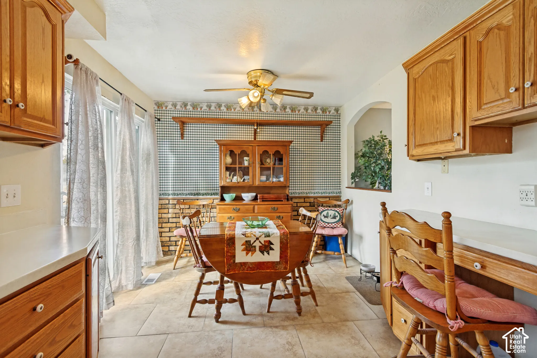 Dining space featuring tile flooring, wood cabinetry, stone-texture wall accents, a multi-light ceiling fan, and sliding glass doors