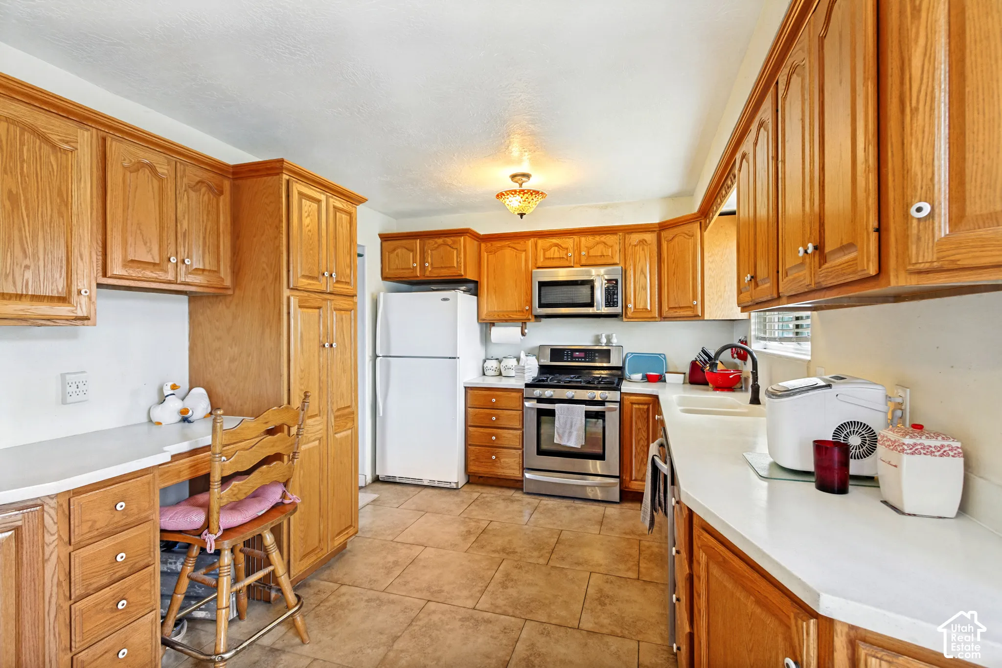 Kitchen featuring wood cabinetry, stainless steel appliances, white countertops, tile flooring, and a built-in desk area