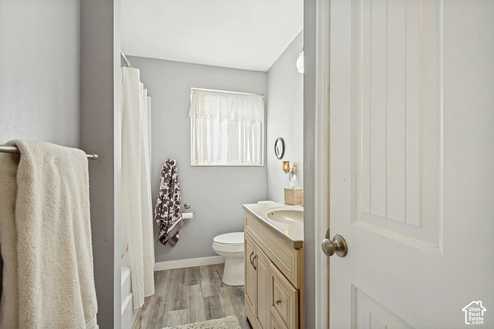 Bathroom featuring wood-finish flooring, a vanity with a neutral countertop and integrated sink, a bathtub and shower combination, and a window