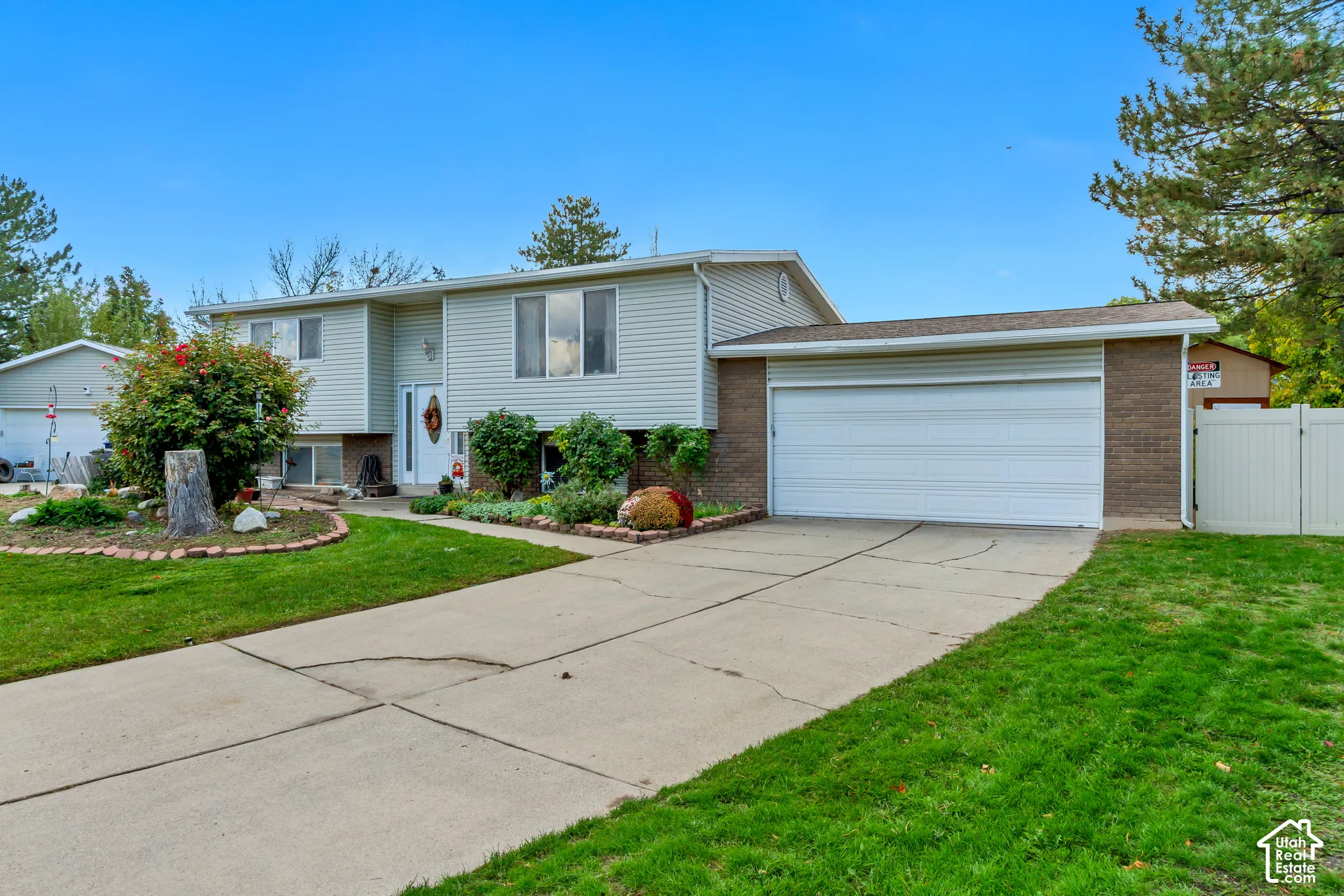 Split-level exterior featuring horizontal siding, brick masonry, an attached two-car garage, concrete driveway, and landscape beds