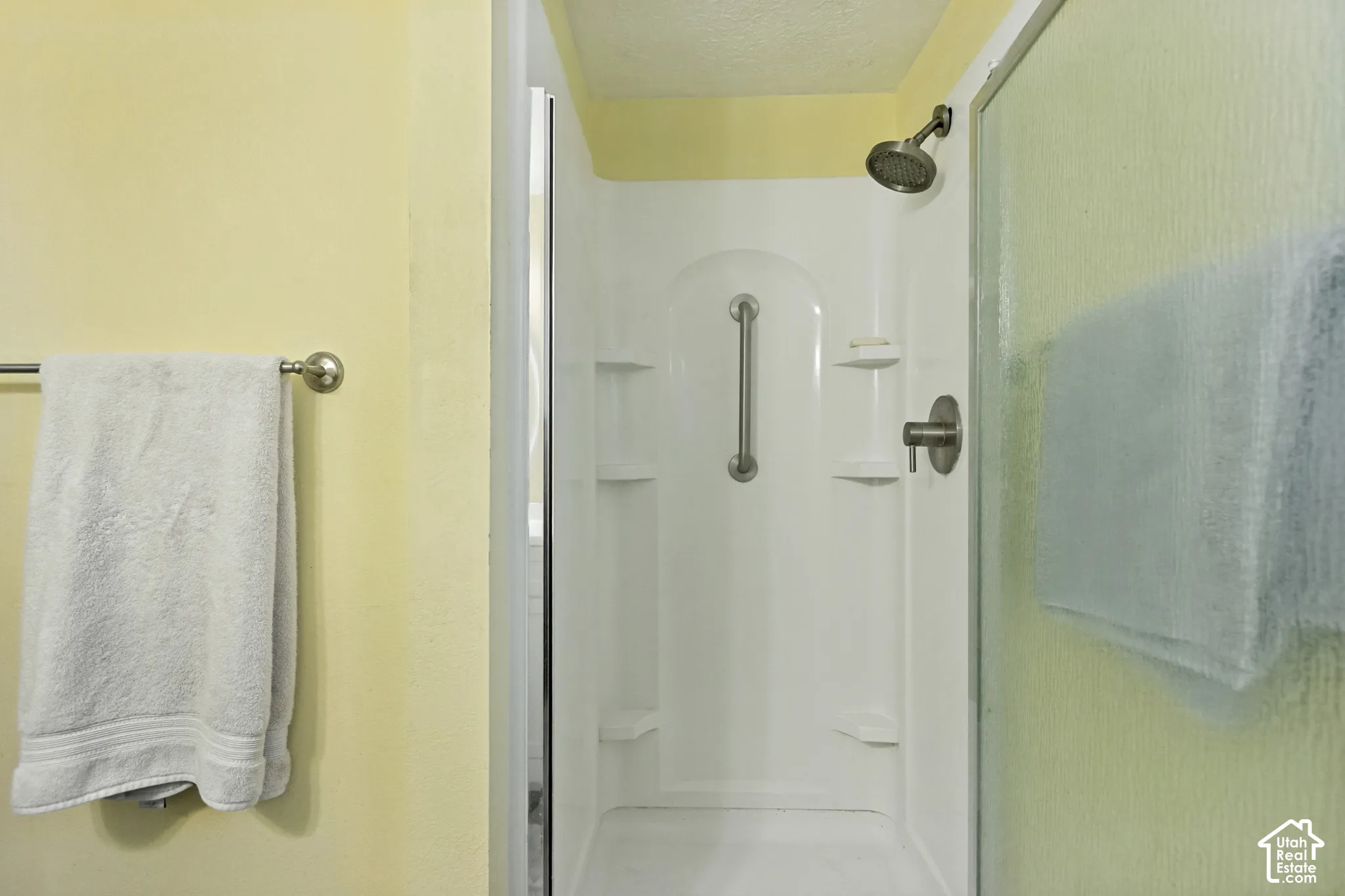 Shower stall featuring a white molded surround with integrated shelving, a stainless steel grab bar, a circular shower head, and a single-handle faucet