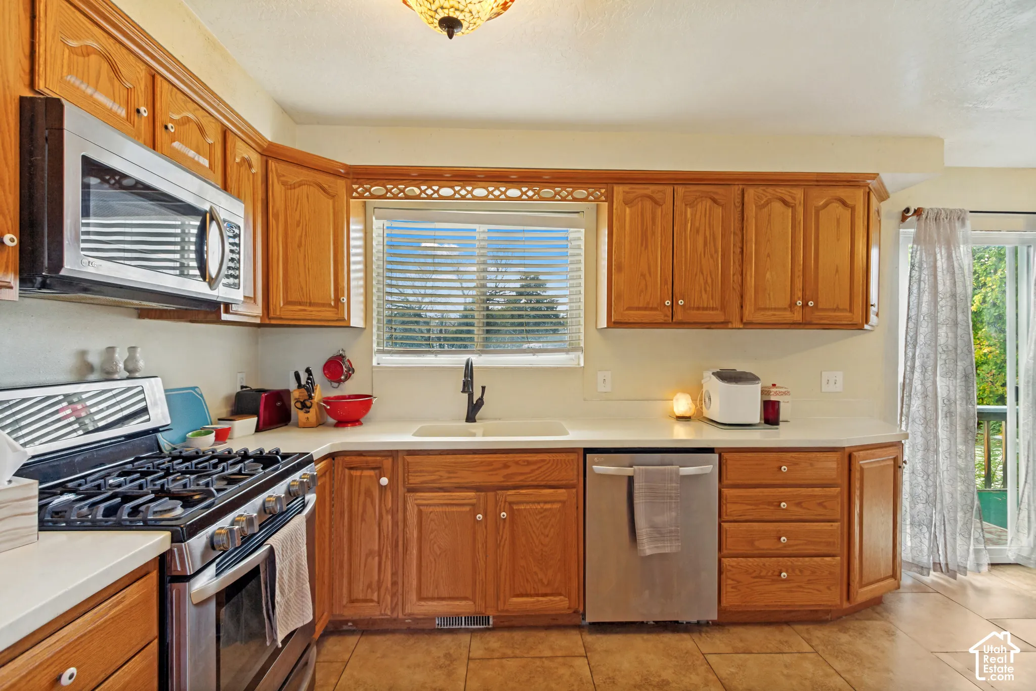 Kitchen featuring oak cabinetry, stainless steel appliances, a white basin sink with a dark-finish faucet, and tile flooring