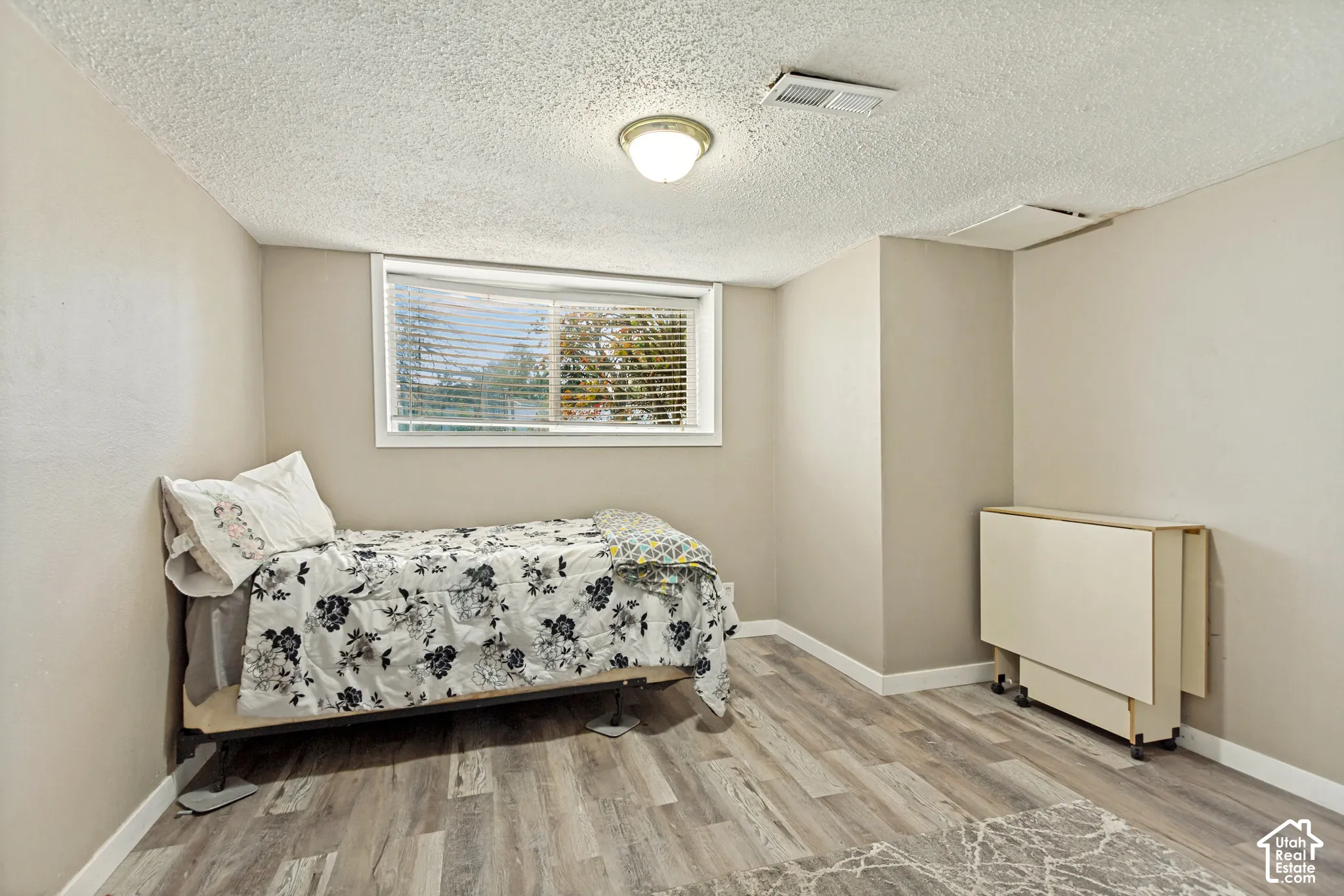 Room featuring wood-finish flooring, a horizontal sliding window with interior blinds, and a flush-mount ceiling light fixture