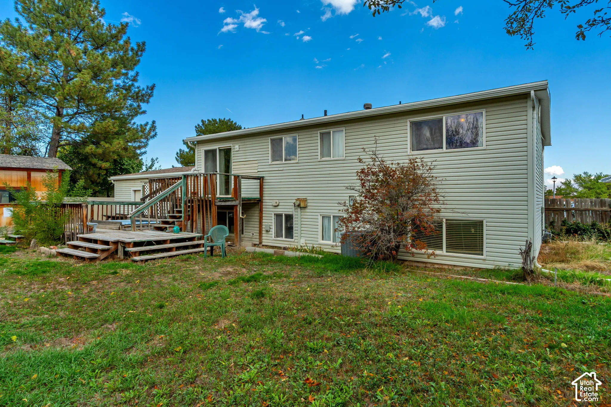 Exterior featuring light-toned horizontal siding, multi-level wood deck, sliding glass door, and mature trees