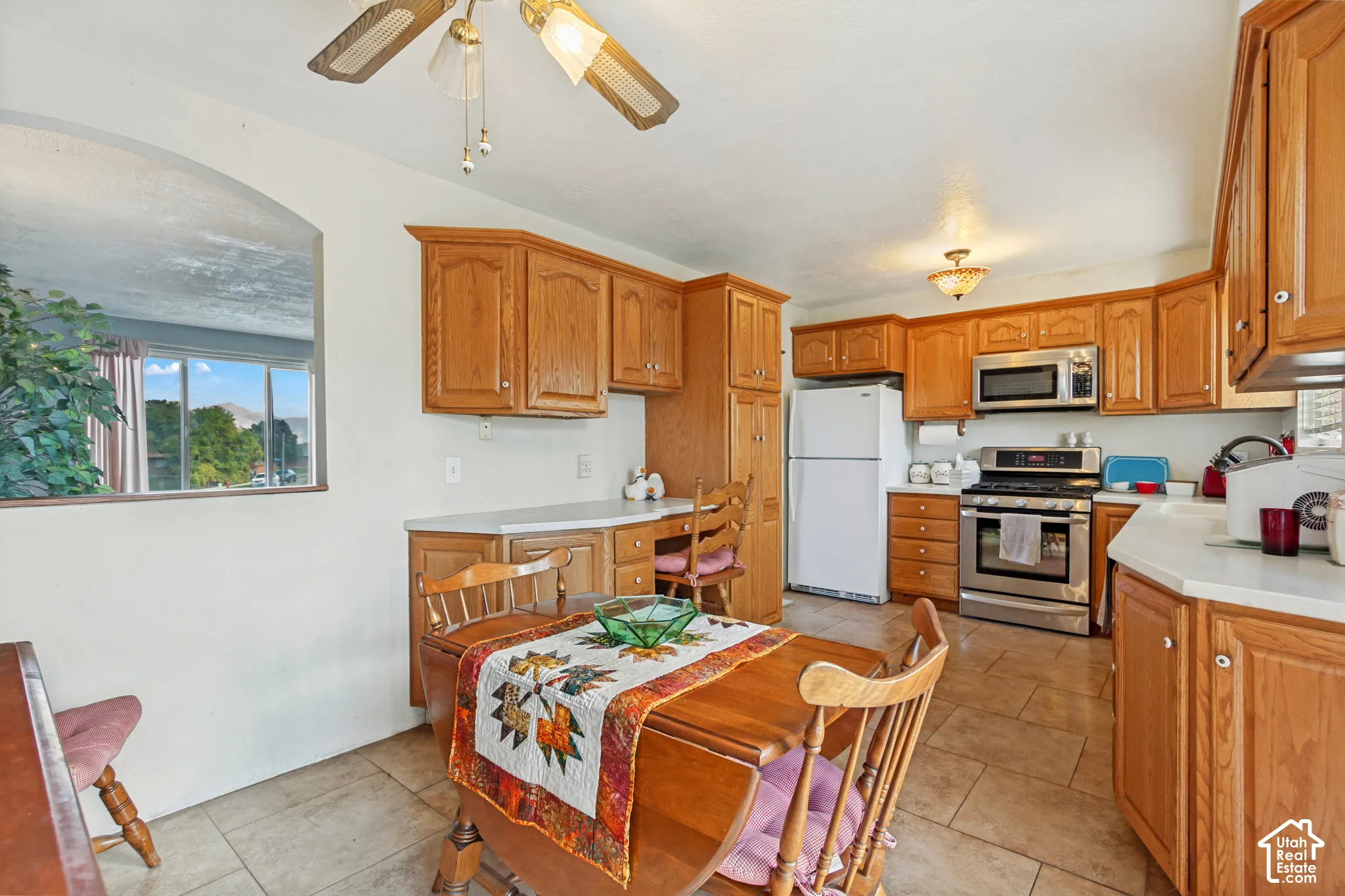 Kitchen featuring oak cabinetry, tile flooring, stainless steel range and microwave, and a built-in desk area