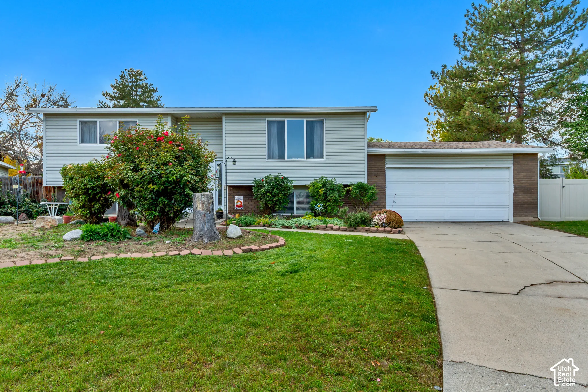 Split-level exterior featuring light horizontal siding, brick facade accents, an attached two-car garage, and a concrete driveway