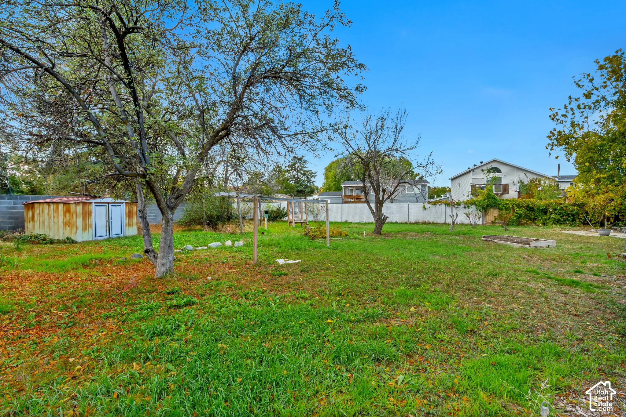 Expansive backyard featuring mature trees, a detached storage structure, perimeter fencing, and designated garden space