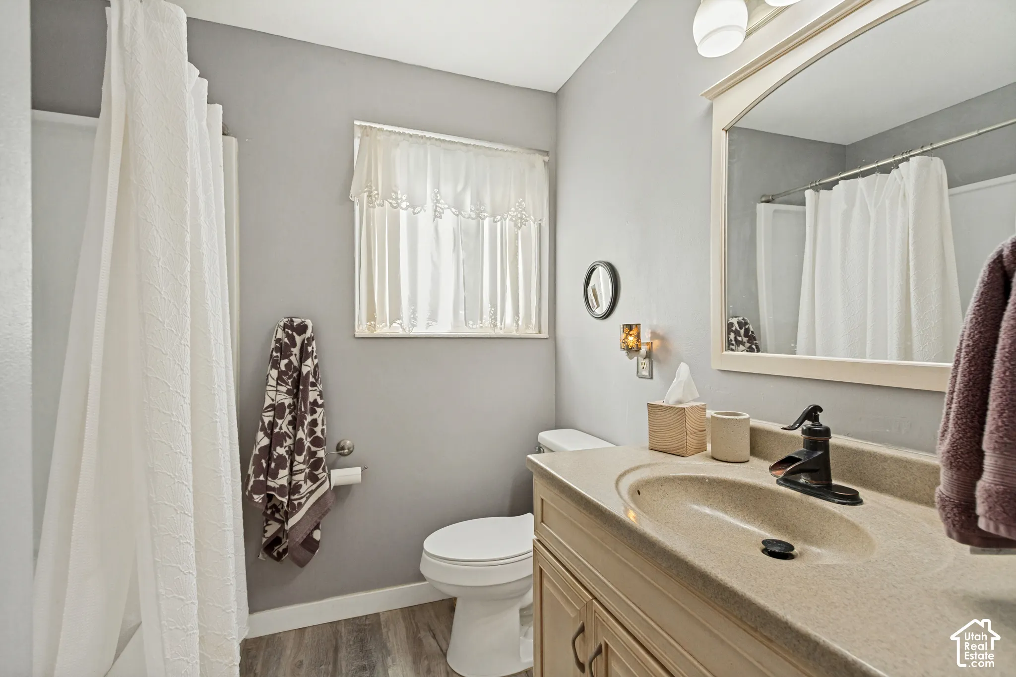 Bathroom featuring a vanity with an integrated basin, a matte black faucet, a framed mirror, and wood-finish flooring