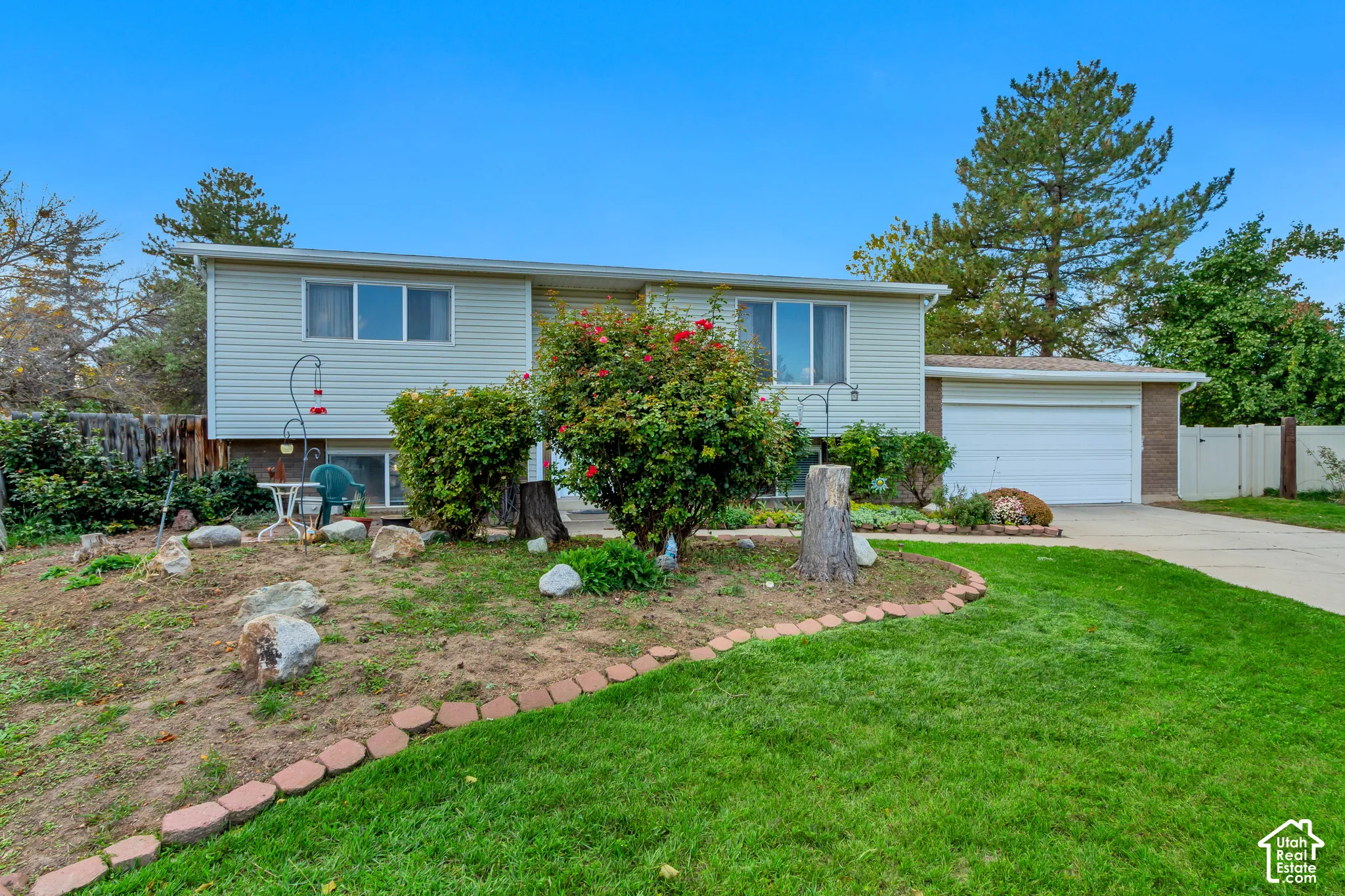 Split-level exterior featuring light-toned horizontal siding, a two-car attached garage, stone landscaping borders, and a paved concrete driveway