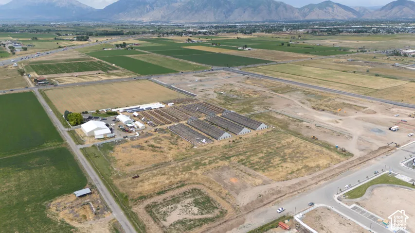 Expansive acreage featuring multiple agricultural structures, metal-roofed buildings, paved access points, and prominent mountain backdrops