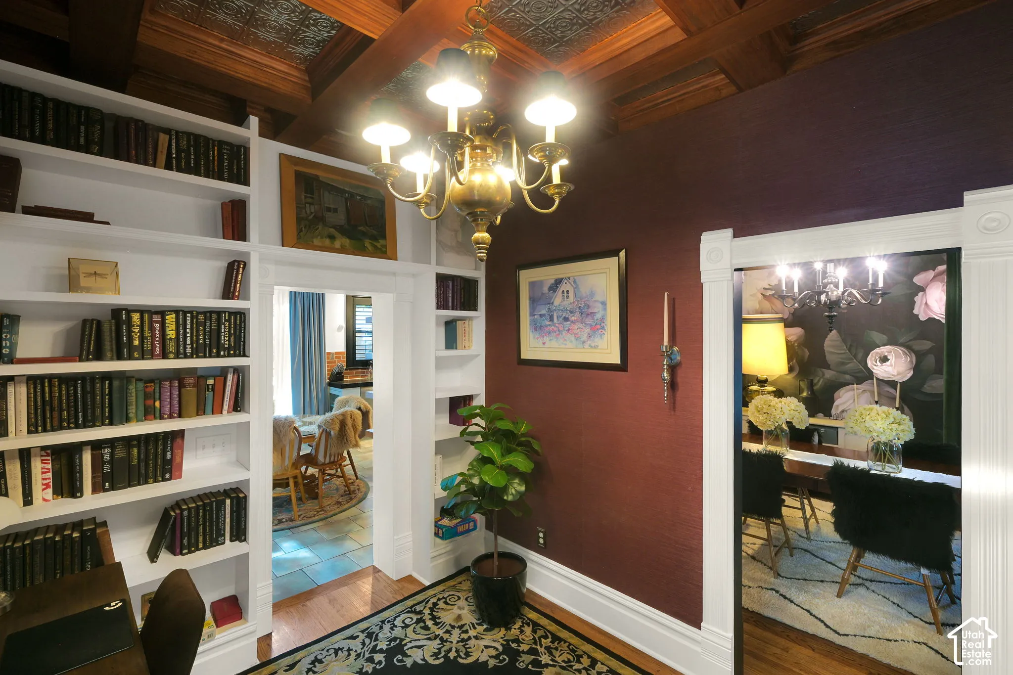 Custom floor-to-ceiling built-in shelving, coffered ceiling with inset metal paneling, and an ornate brass chandelier