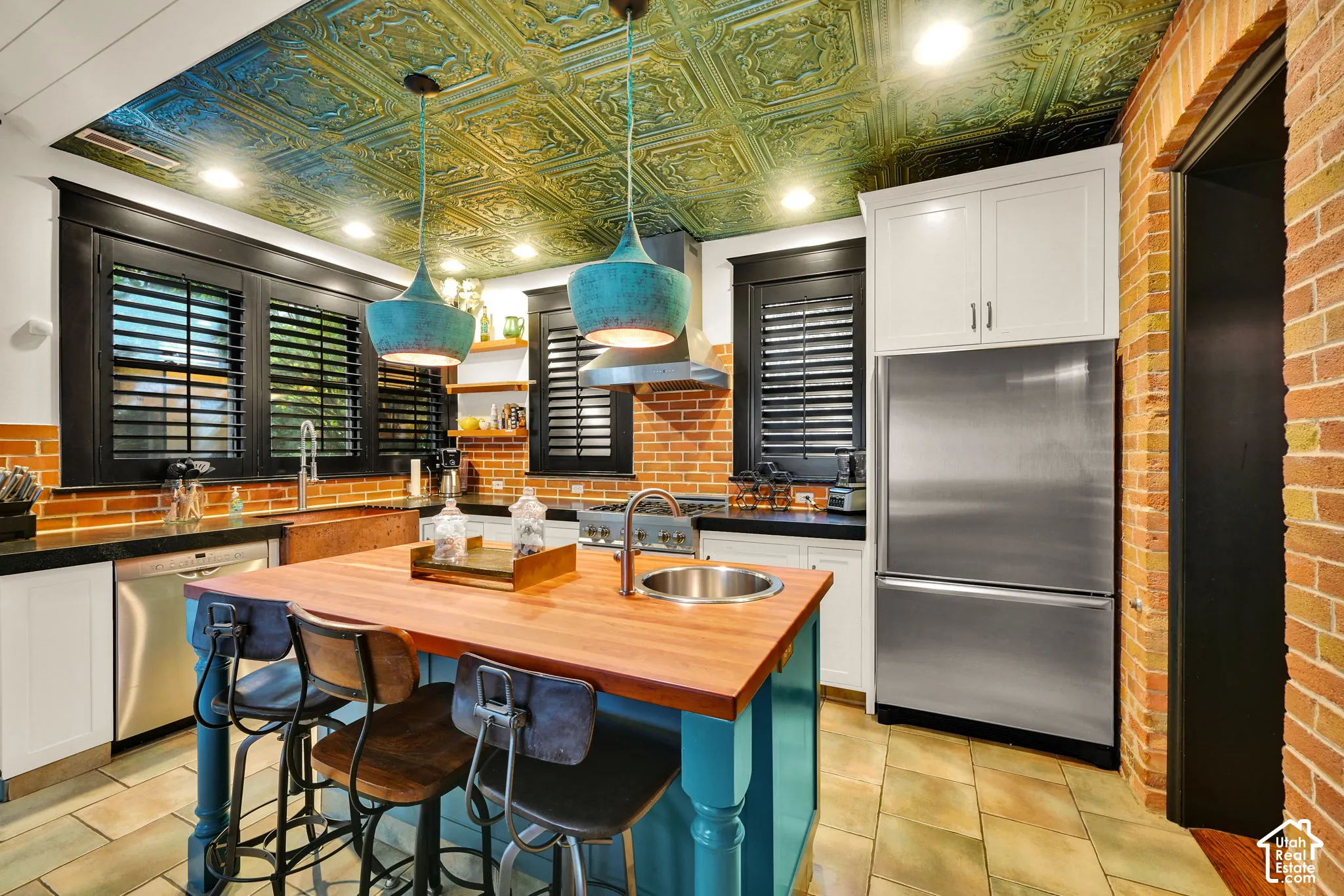 Kitchen featuring a decorative pressed tin ceiling, exposed brick walls, a center island with a wood countertop and integrated circular prep sink, and custom cabinetry with dark-finish window casings