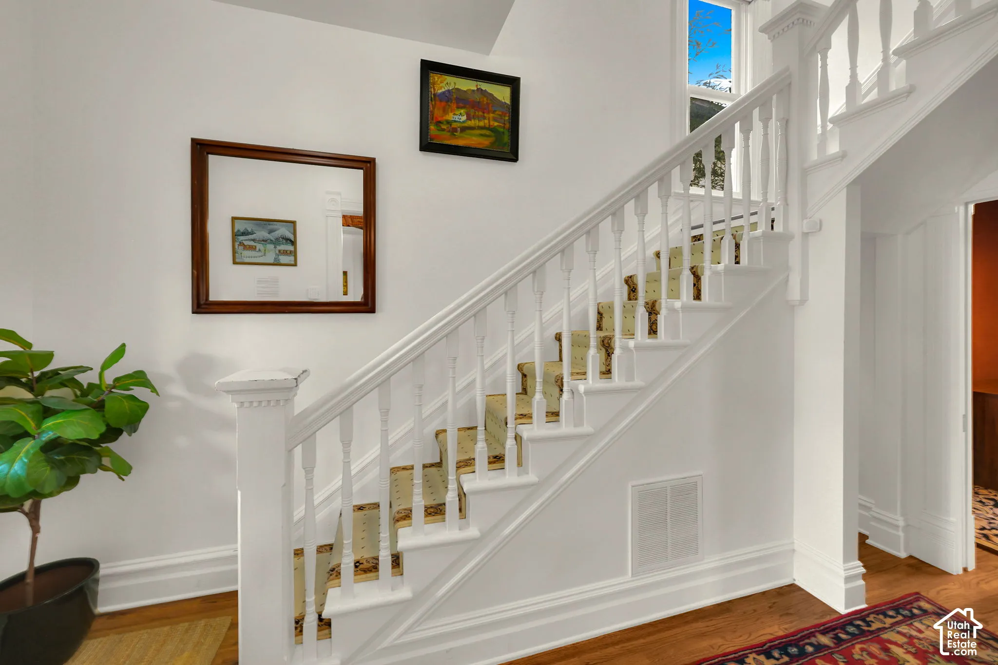 Staircase featuring white-painted wood balusters, a square newel post, and patterned stair runner, complemented by wood-finish flooring
