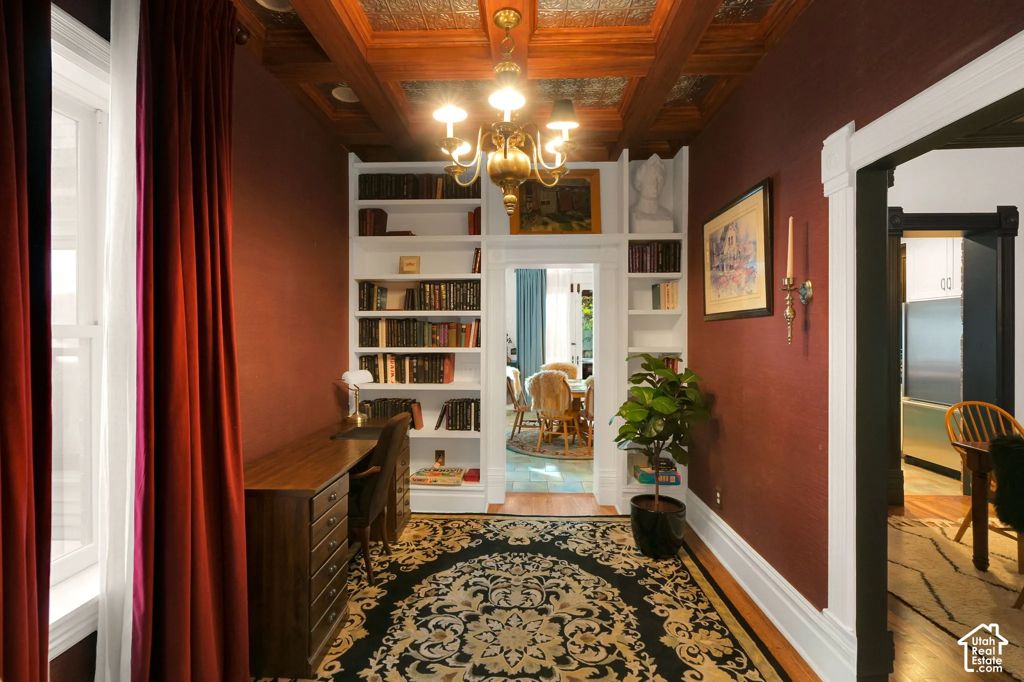 Coffered ceiling with decorative tin inserts, built-in floor-to-ceiling shelving, central chandelier, and solid-wood casing