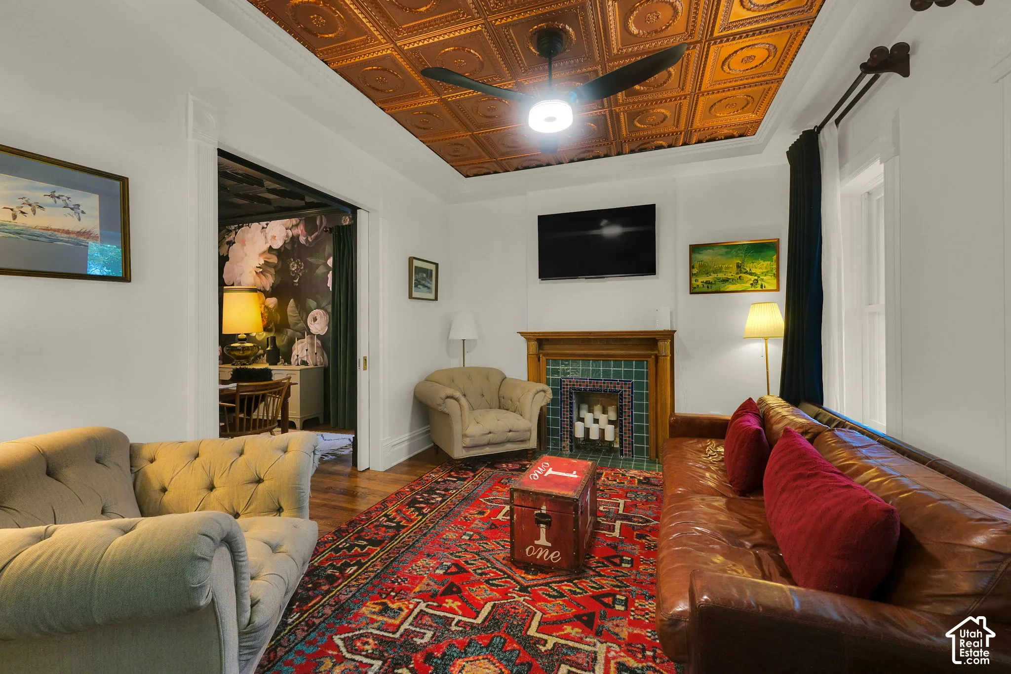 Detailed coffered-style metallic ceiling tiles, wood-finish flooring, and a fireplace featuring a natural wood mantel and tiled surround