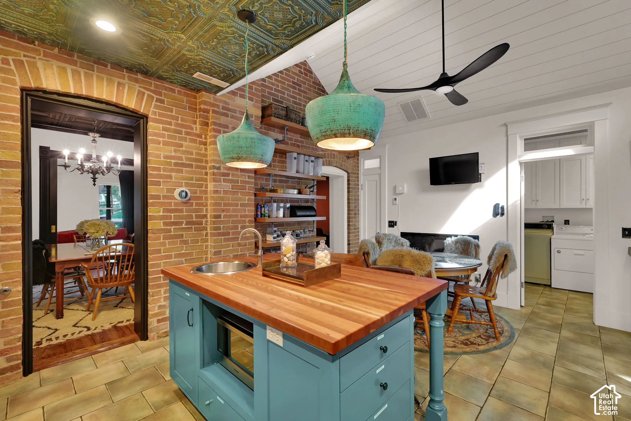 Exposed brick walls, custom center island with butcher block countertop, decorative patterned metal ceiling, pendant lighting, and ceramic tile flooring
