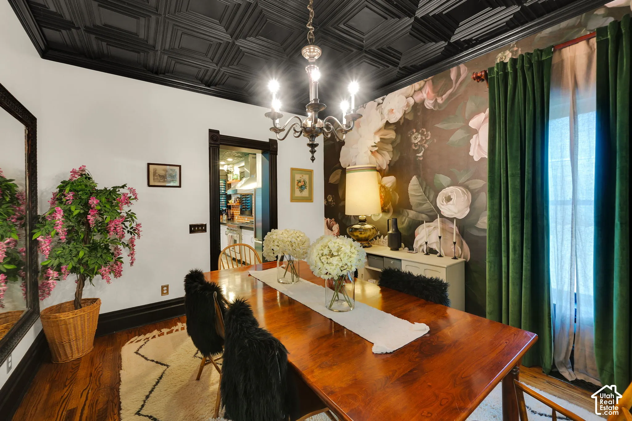 Black coffered ceiling, floral wall covering, polished wood-finish flooring, dark-stained door casing, and ornate chandelier
