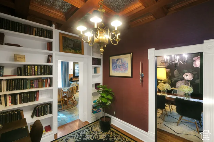 Custom floor-to-ceiling built-in shelving, coffered ceiling with inset metal paneling, and an ornate brass chandelier