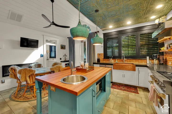 Kitchen featuring a centerpiece island with a wood countertop, copper farmhouse sink, exposed brick backsplash, patterned metallic ceiling, and built-in gas range