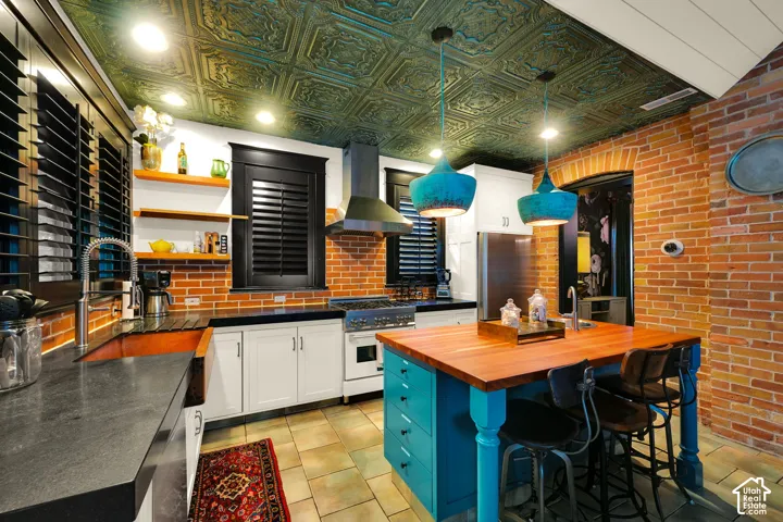 Kitchen featuring an ornate metallic-finish ceiling, exposed brick walls, and a center island with a butcher-block countertop