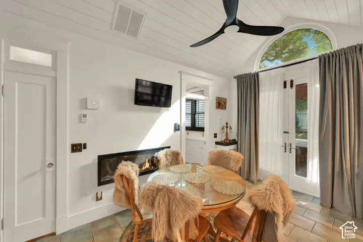 Vaulted ceiling with shiplap detail, stone tile flooring, linear electric fireplace, matte black ceiling fan, and arched transom window above glass-paneled double doors