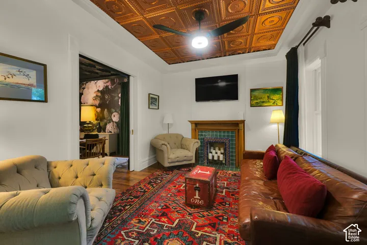 Detailed coffered-style metallic ceiling tiles, wood-finish flooring, and a fireplace featuring a natural wood mantel and tiled surround