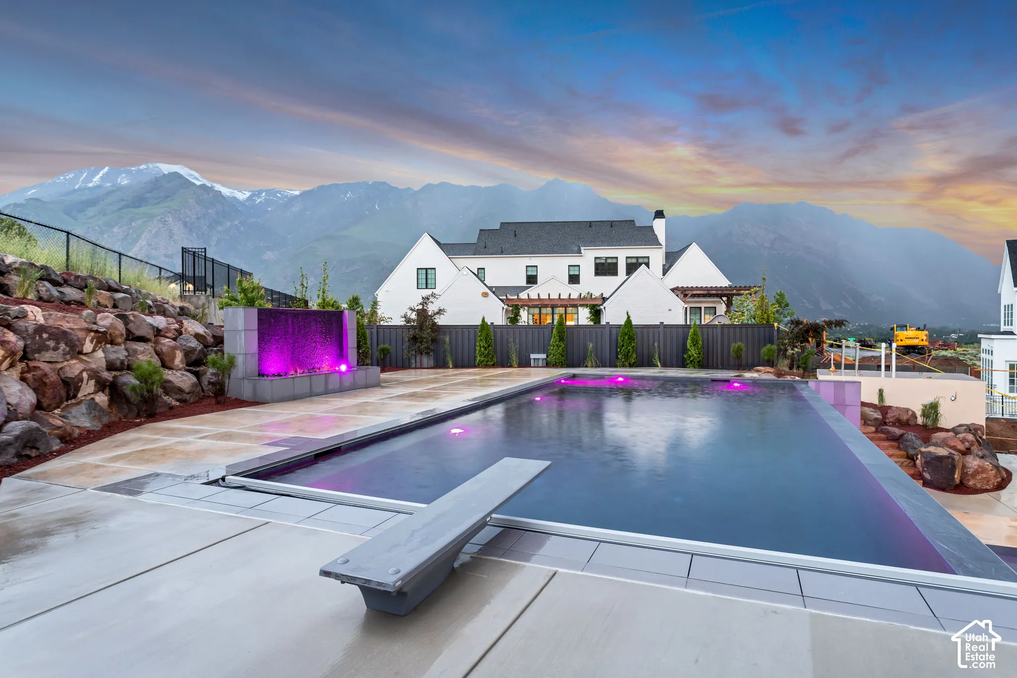 Swimming pool with a diving board, stone-retaining wall, water feature, concrete hardscaping, and mountain backdrop