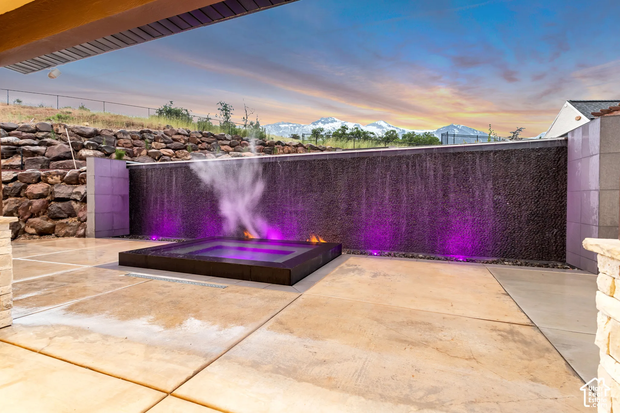 Outdoor patio featuring a tiered rock retaining wall, built-in water feature with integrated lighting, recessed spa, and mountain backdrop