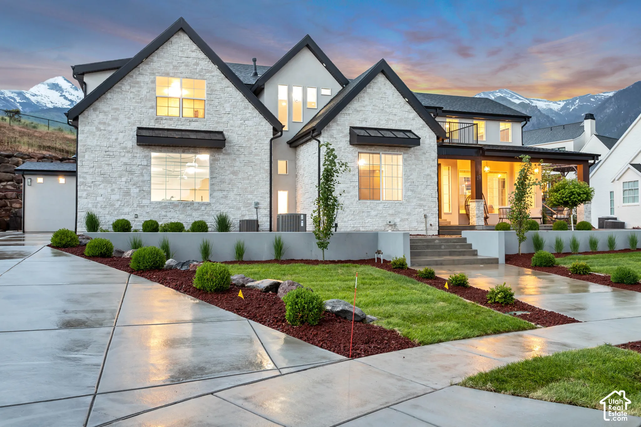 Custom stone veneer facade featuring multi-gabled rooflines, dark metal awning accents, covered porch, and concrete driveway against a mountain backdrop