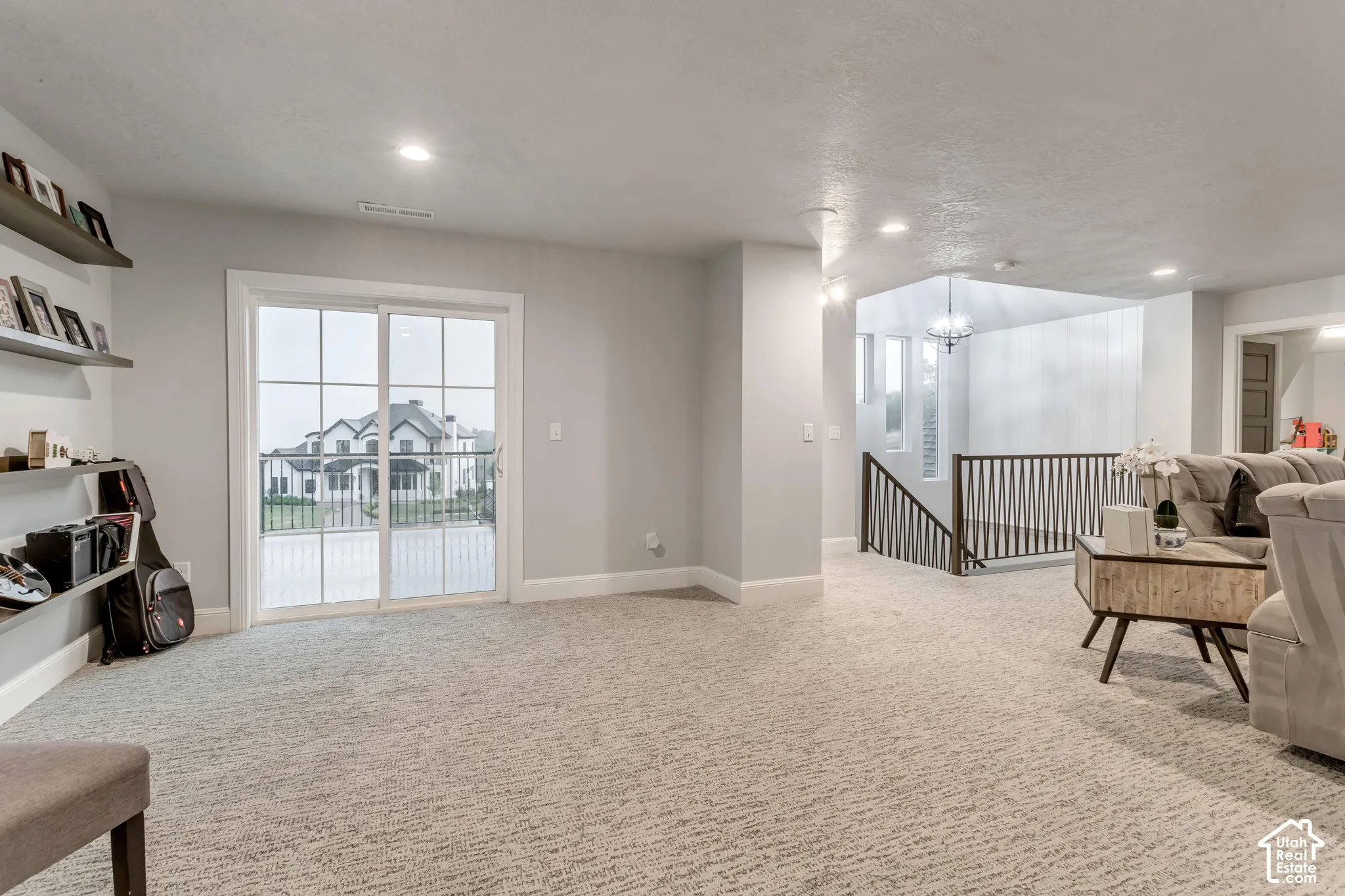 Open-concept interior featuring wall-to-wall carpeting, recessed lighting, built-in wall shelving, and glass sliding doors leading to an exterior balcony with metal railings