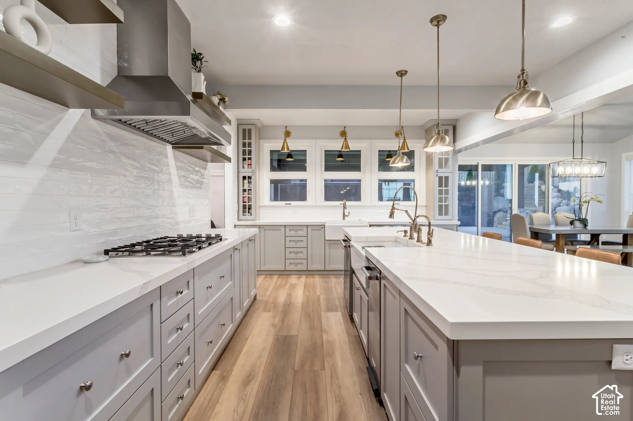 Kitchen featuring wood-finish flooring, white stone-surface countertops, shaker-style cabinetry, a stainless steel range hood, and a farmhouse-style apron sink