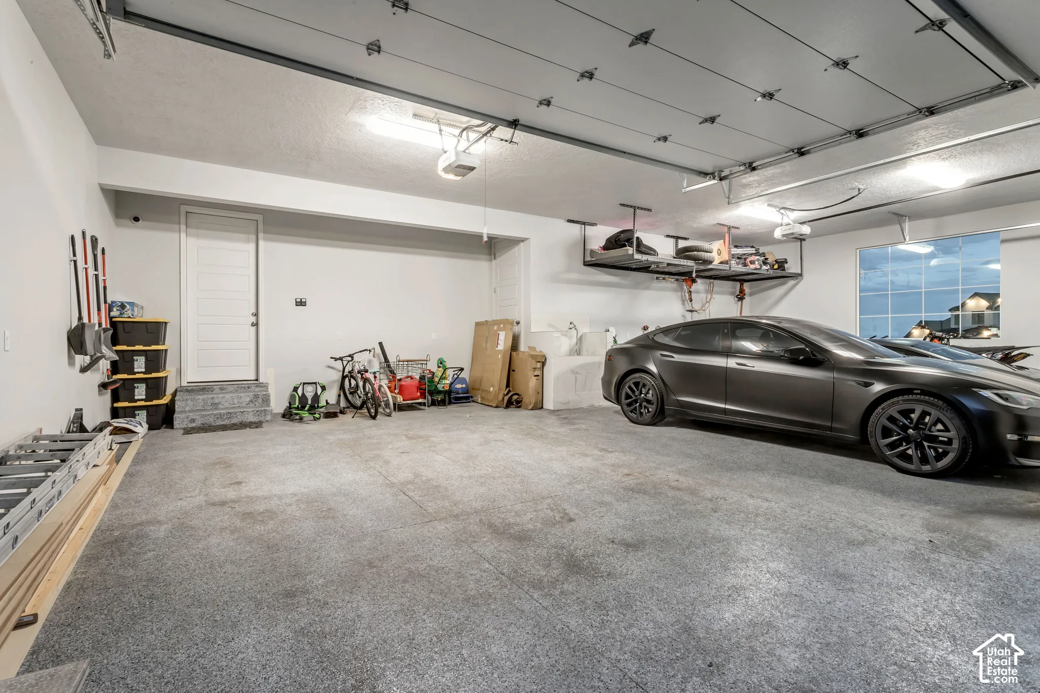 Multi-car garage featuring epoxy flooring, built-in overhead storage racks, a utility sink, and an exterior access door