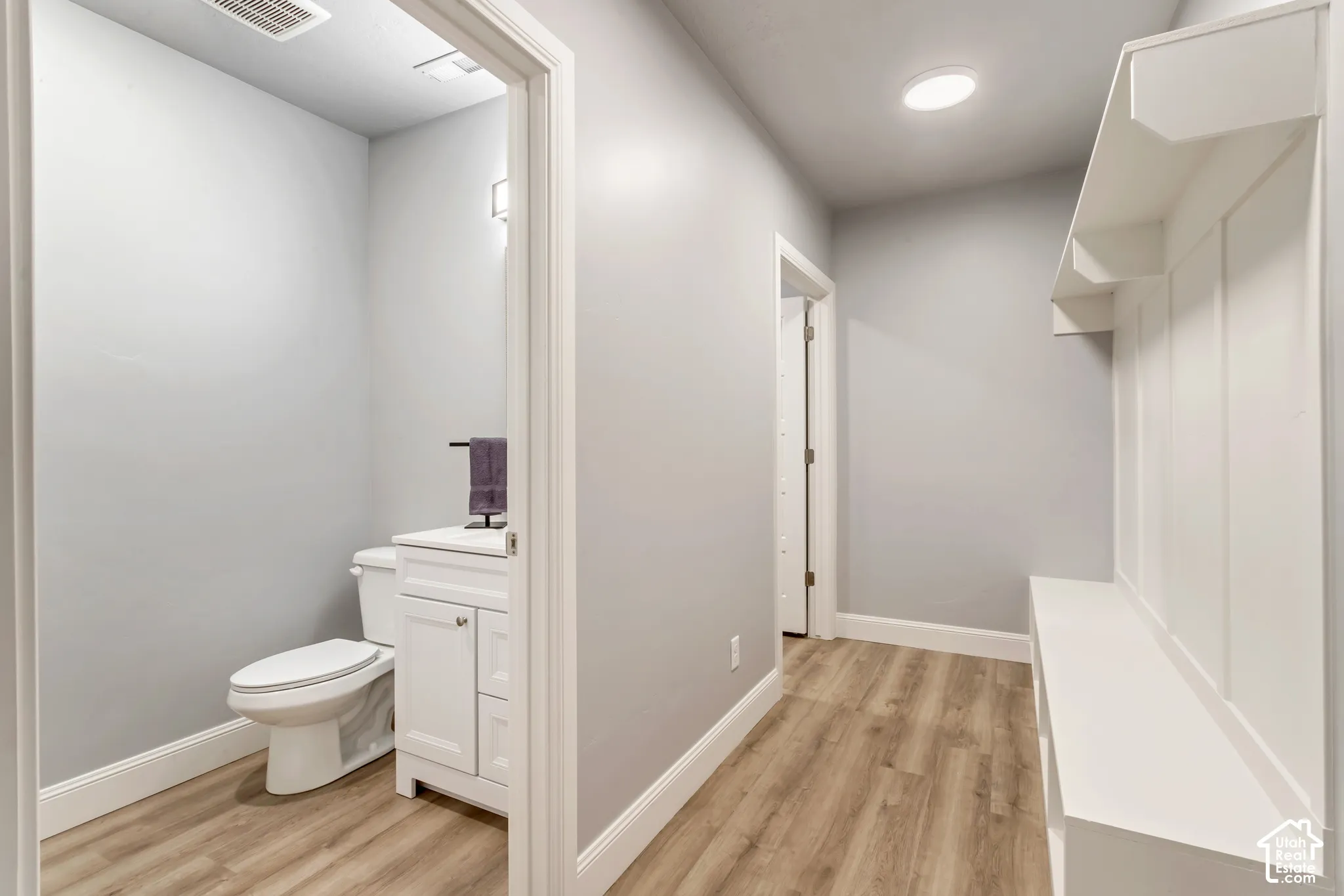 Wood-finish flooring, built-in mudroom bench with overhead storage, white shaker-style vanity, and flush-mount LED lighting