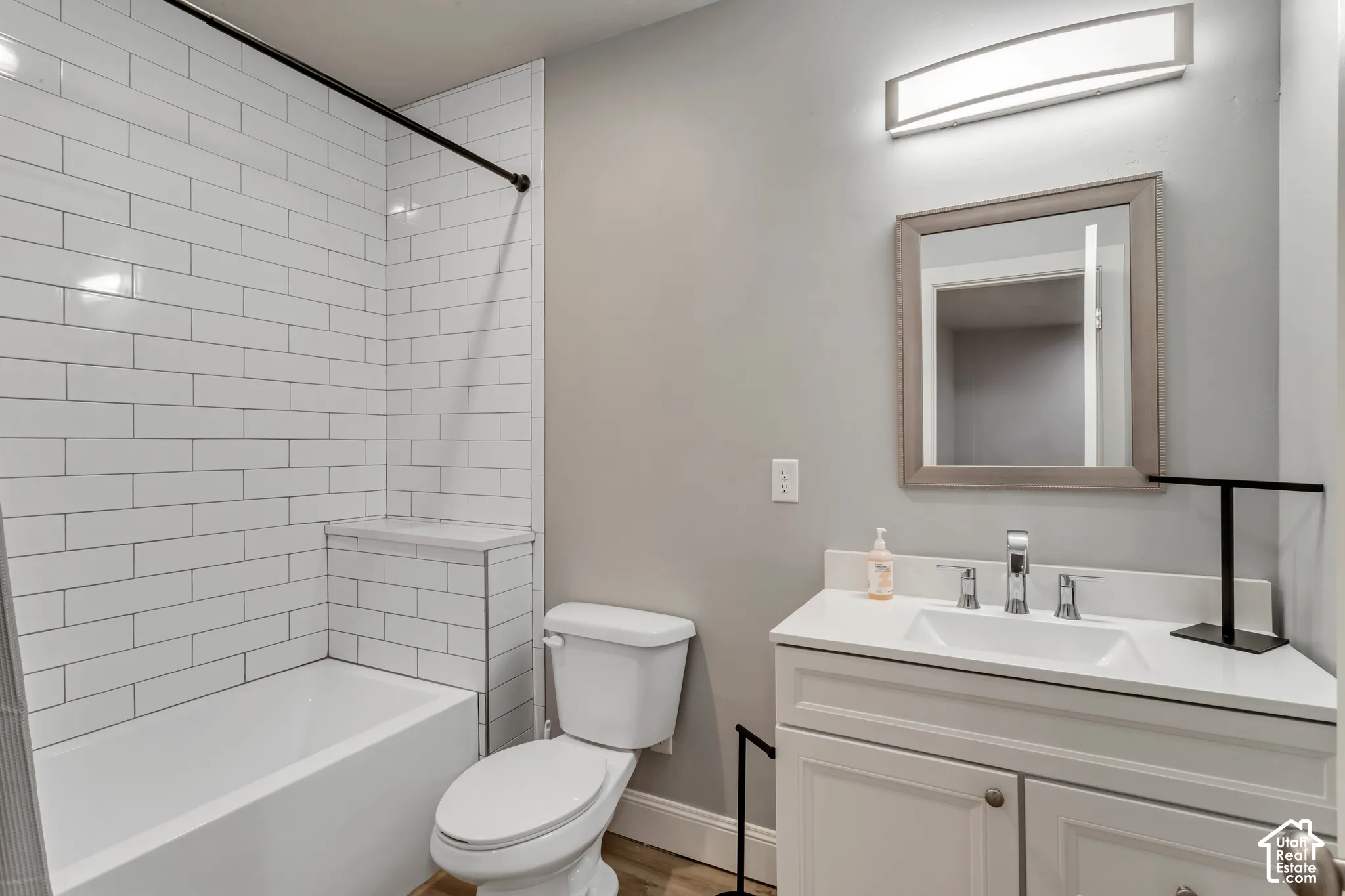 Bathroom featuring white subway tile tub surround, white vanity with integrated basin, polished metal faucet, rectangular wall-mounted light fixture, and framed mirror
