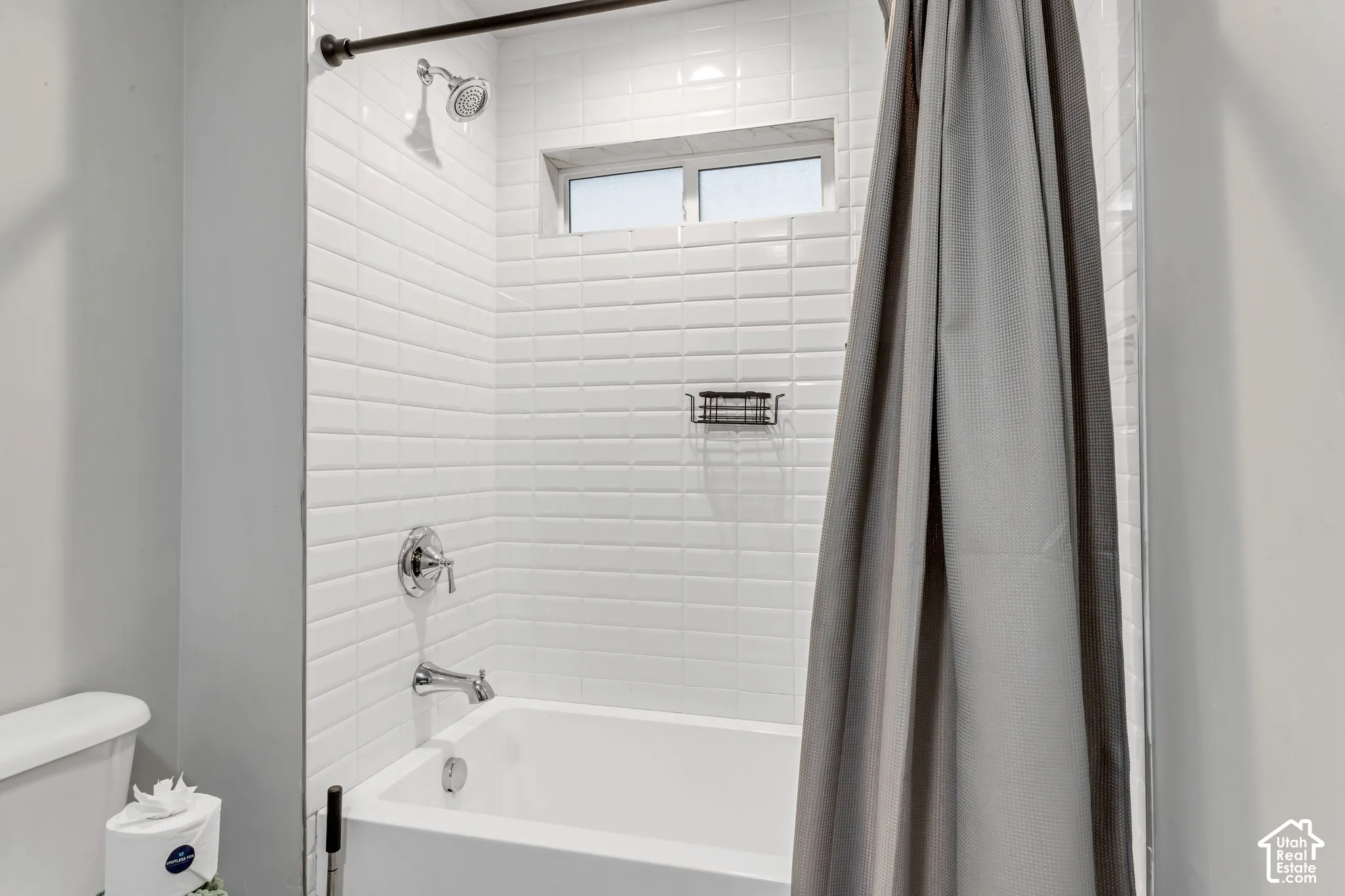 Tub and shower combination featuring white subway tile surround, chrome faucet fixtures, an integrated recessed niche, and a horizontal transom window