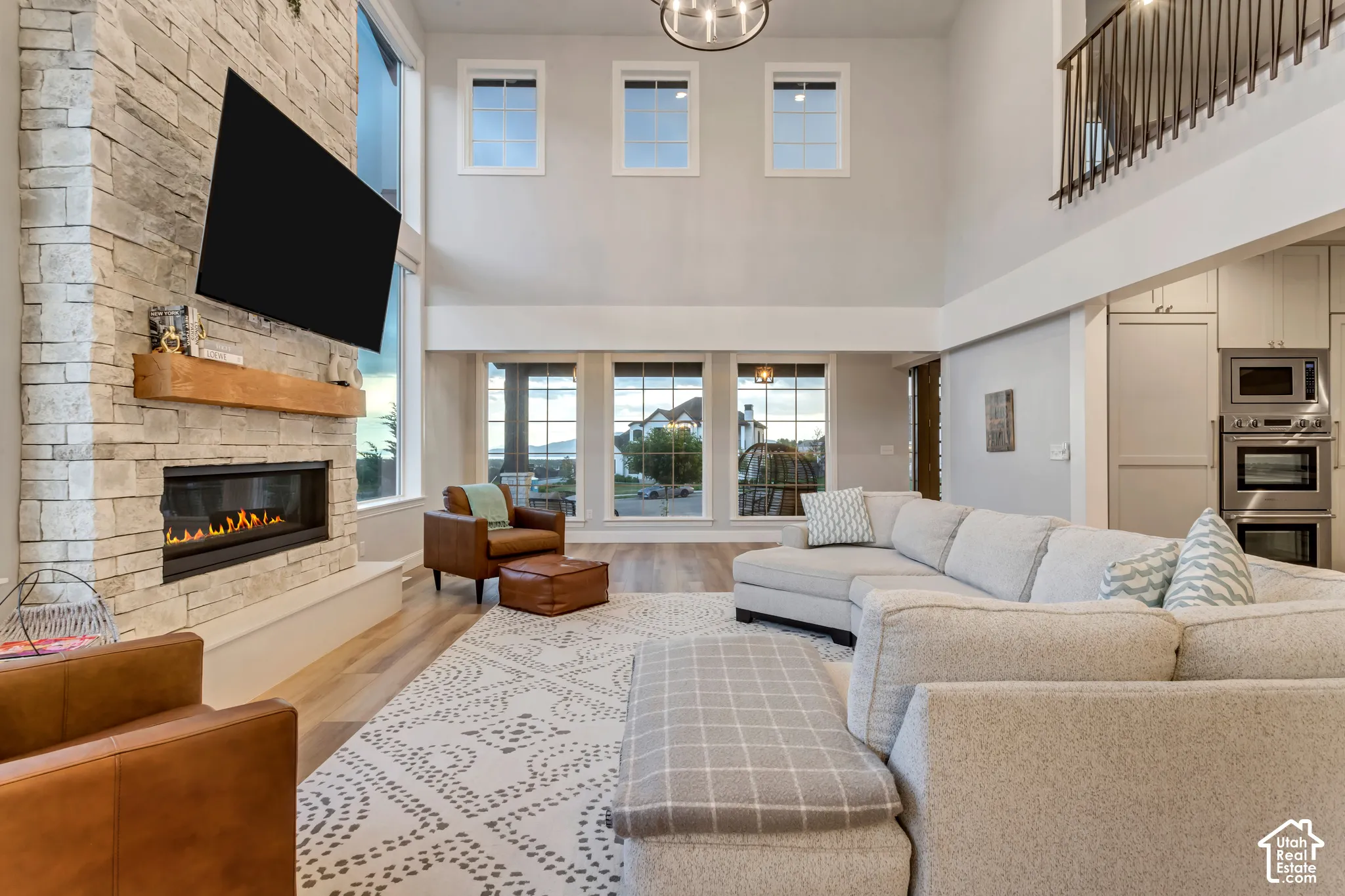 Two-story living area featuring a floor-to-ceiling stone fireplace, linear hearth, rustic wood mantel, expansive windows, and wood-finish flooring