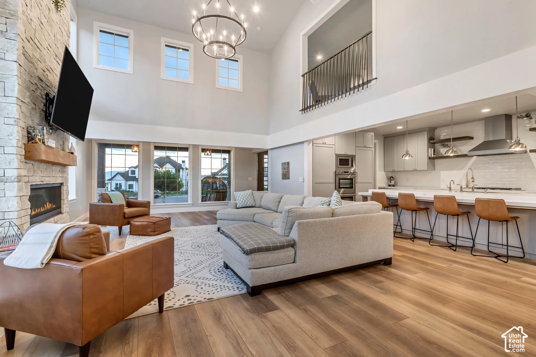 Vaulted ceilings featuring a floor-to-ceiling stone fireplace, wood-finish flooring, a large kitchen island with pendant lighting, and a metal-railed interior balcony