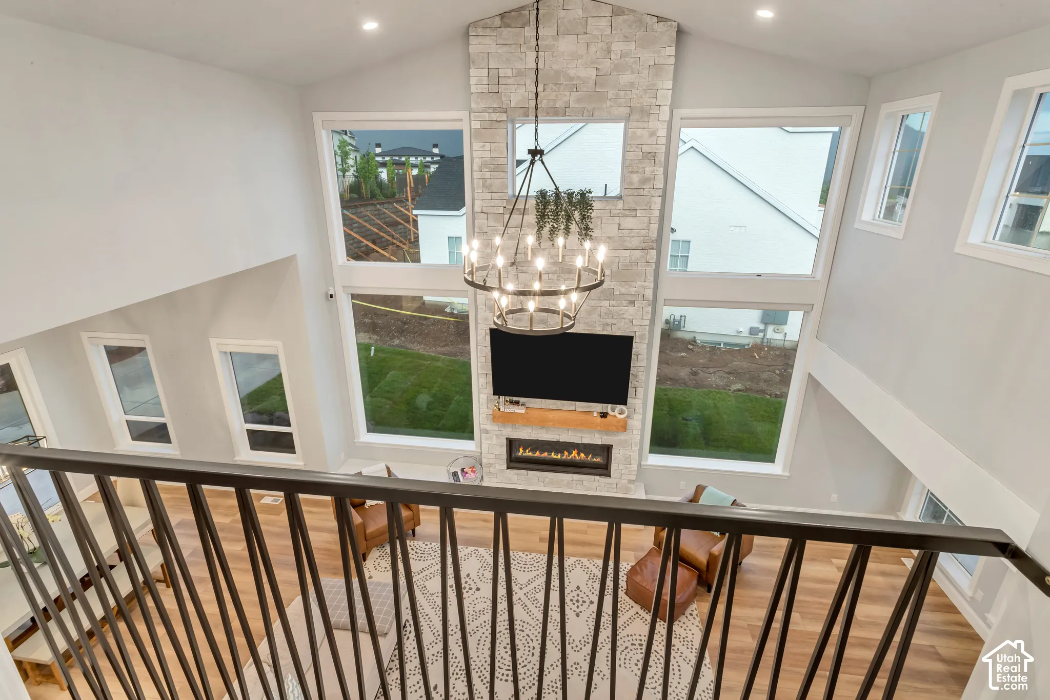 Vaulted ceiling with a full-height stone-clad fireplace, linear built-in electric fireplace, metal spindle railing, and oversized windows