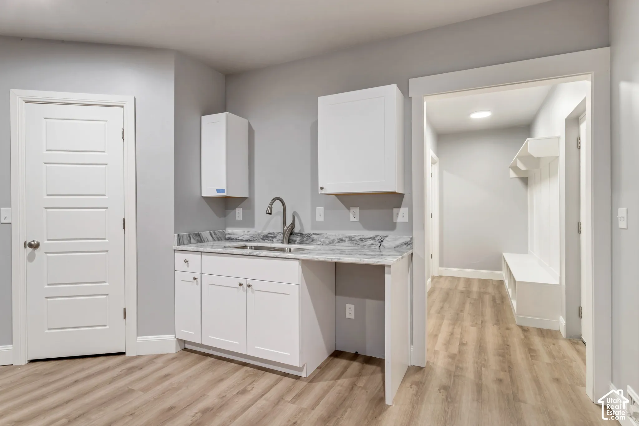 Laundry room featuring white cabinetry, stone-patterned countertop, integrated sink with gooseneck faucet, wood-finish flooring, and built-in mudroom bench with shelving