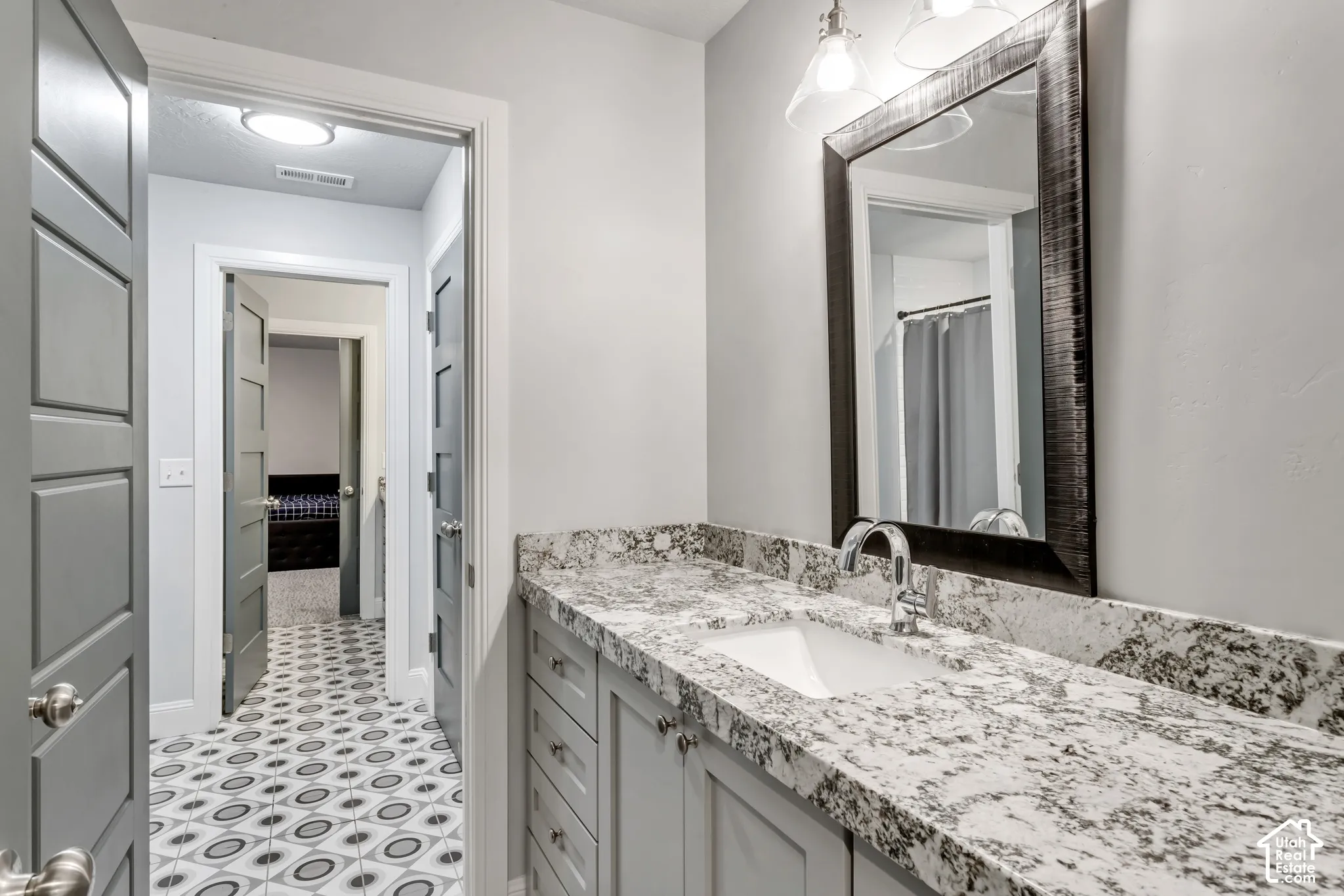 Bathroom vanity featuring a stone-patterned countertop, undermount sink, chrome faucet, shaker-style cabinetry, and a framed mirror