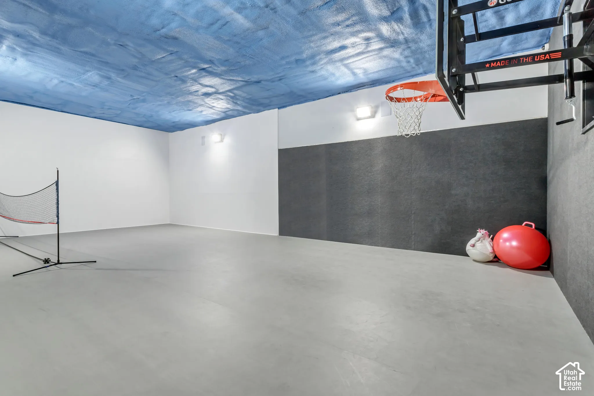Multipurpose recreational area featuring smooth concrete flooring, wall-mounted acoustic panels, spray-textured ceiling finish, and dual wall-mounted light fixtures