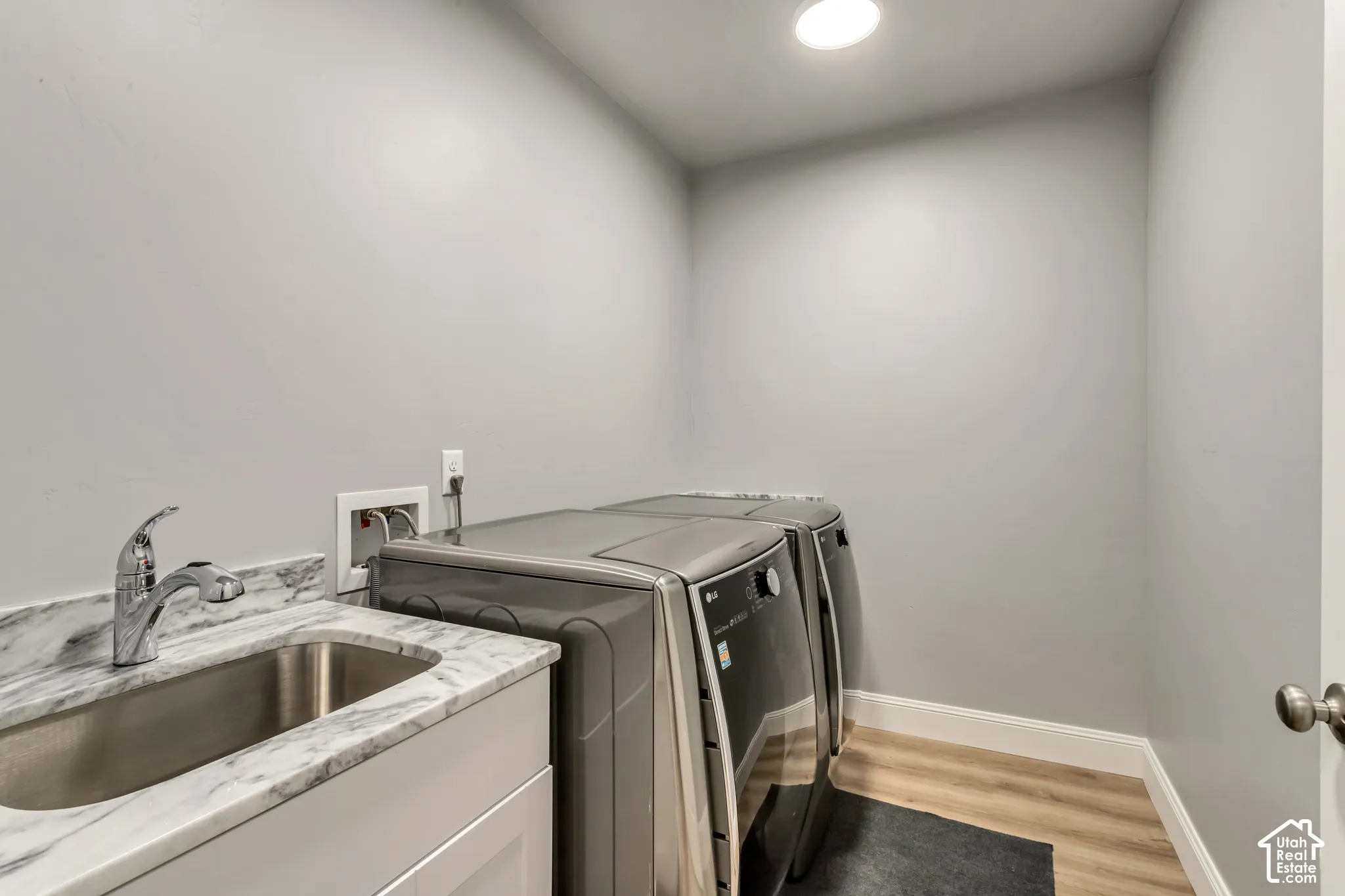 Utility room featuring a stone-finish countertop, stainless steel undermount sink with a high-arch chrome faucet, white cabinetry, and wood-finish flooring