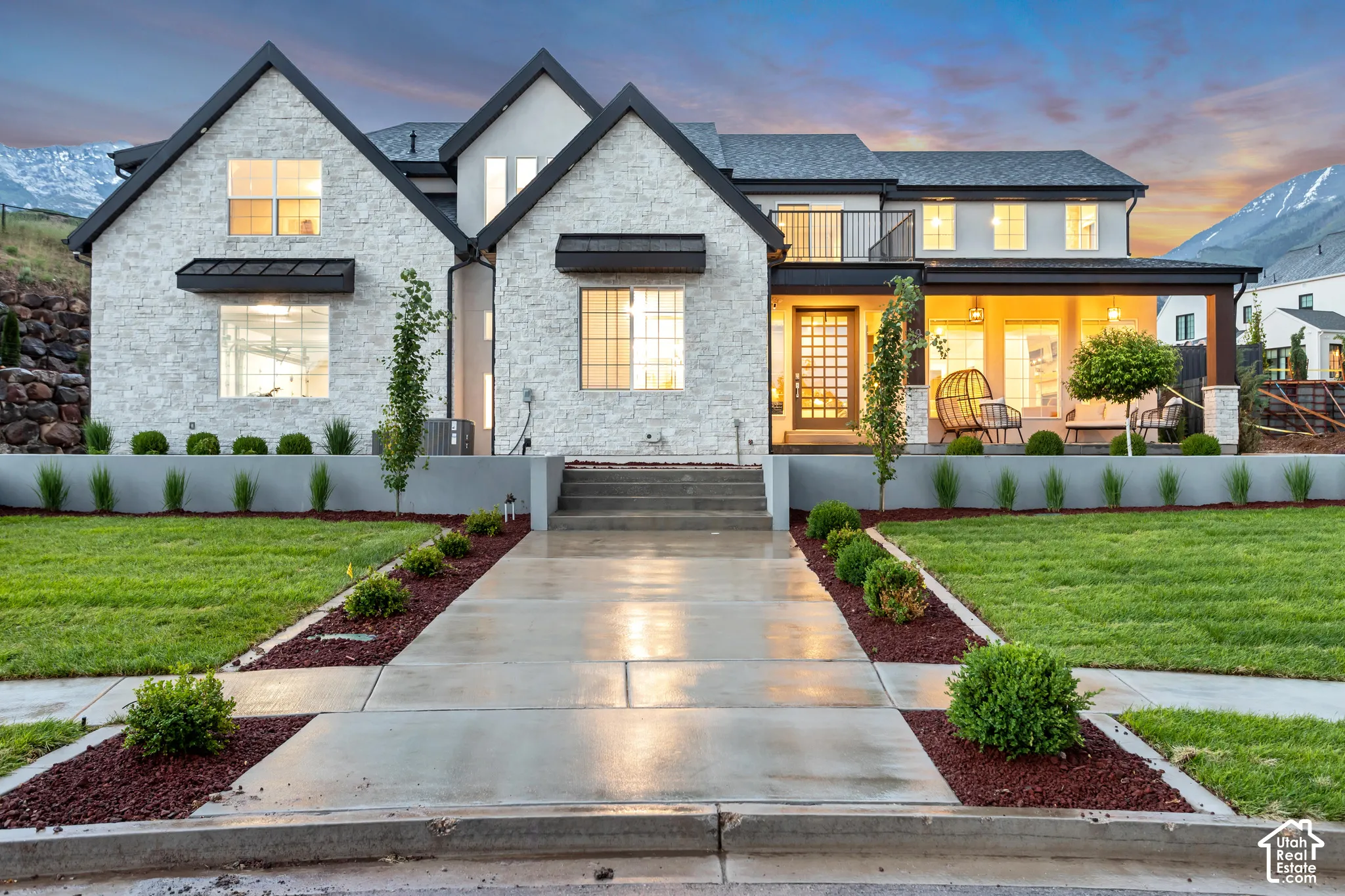 Multi-gabled exterior featuring textured stone veneer, black metal awning accents, covered front porch, and an elevated terrace with a black metal railing