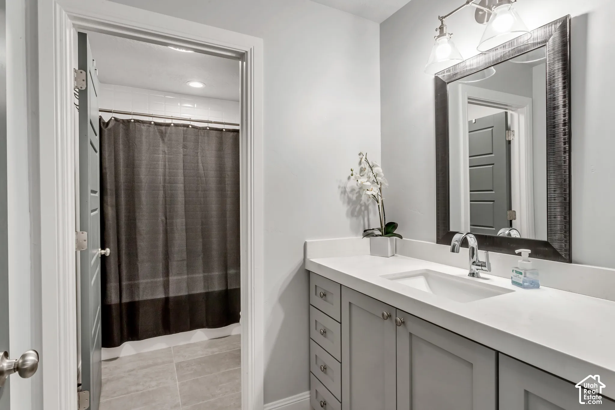 Bathroom featuring a grey vanity with stone-finish countertop, integrated undermount sink, three-light fixture, and ceramic tile flooring