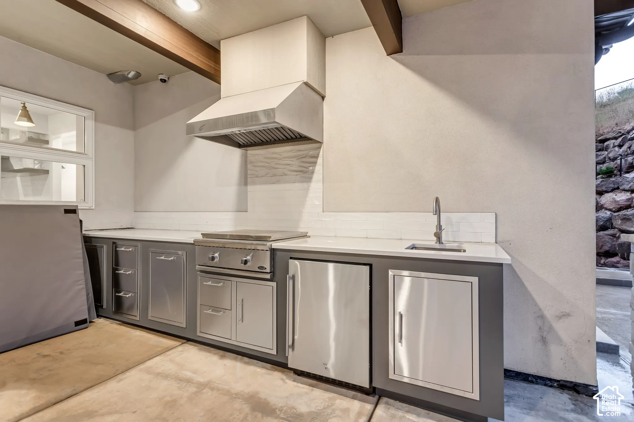 Outdoor kitchen featuring stainless steel cabinetry, a built-in cooktop, integrated ventilation hood, stone-finish countertops, and an undermount sink