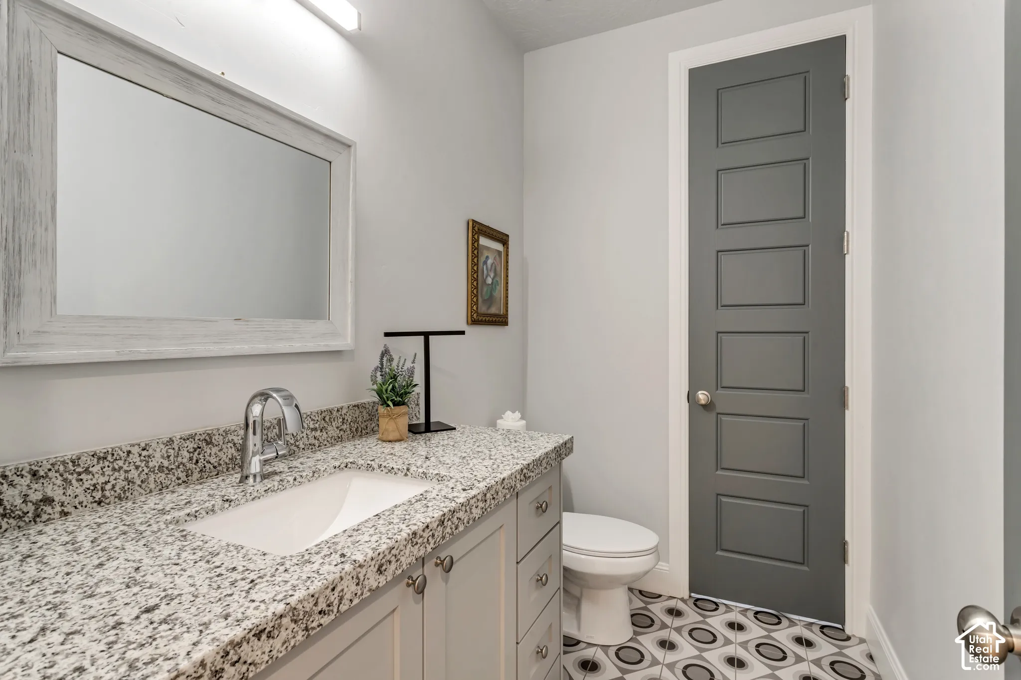 Bathroom featuring a vanity with stone-finish countertop, under-mount sink, high-arc polished chrome faucet, patterned floor tile, and six-panel interior door